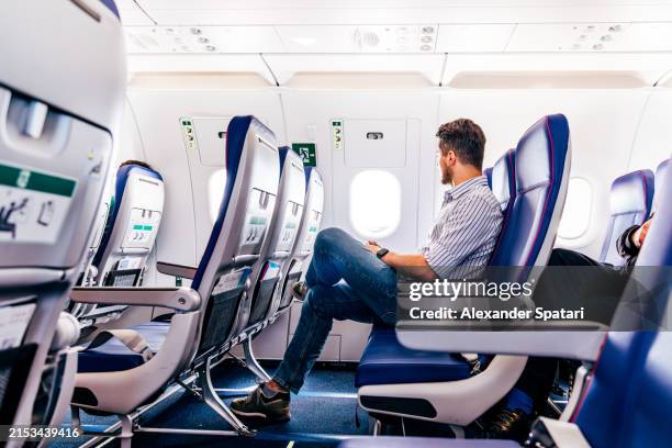 male passenger in smart casual clothing flying in the exit row on an airplane - airplane seat stock pictures, royalty-free photos & images