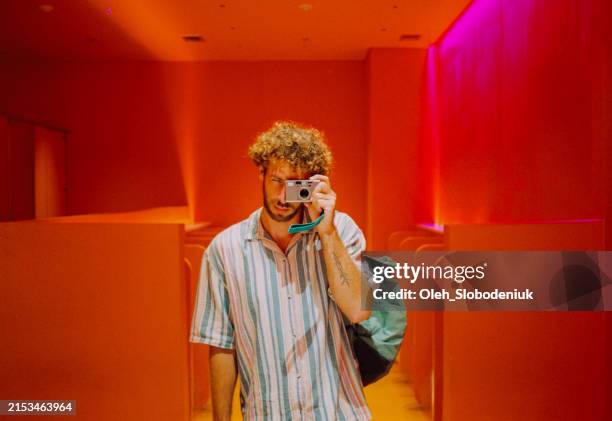 selfie of man in the mirror with film camera in neon lit orange public toilet - man-mirror-selfie stock pictures, royalty-free photos & images