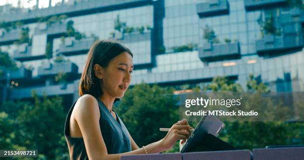 primer plano de dos jóvenes empresarias asiáticas que se reúnen para discutir estratégicamente en la mesa fuera de un moderno edificio de oficinas. negocio sostenible al aire libre. - empresa de carácter social fotografías e imágenes de stock