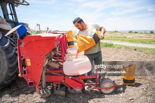 young farmer adding corn seeds to the seeder in the field - sowing machine stock pictures, royalty-free photos & images