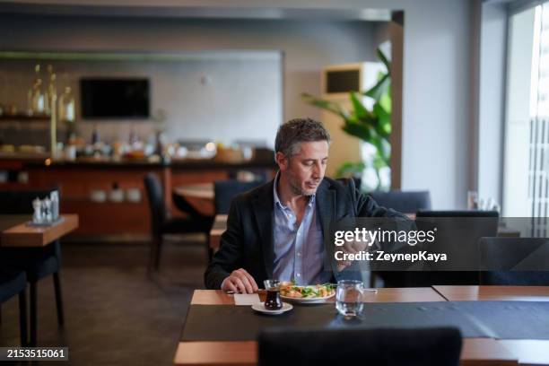 ein mann schaut auf seiner uhr auf die uhr, sitzt auf dem frühstückstisch. - tageszeit stock-fotos und bilder