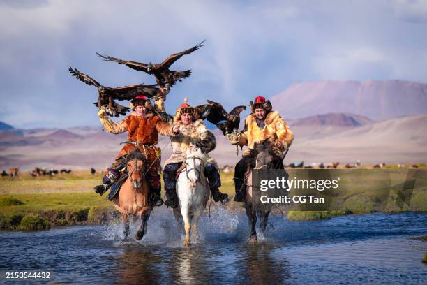 group of kazakh eagle hunters riding horses crossing river bayan olgii, west mongolia - mongoolse etniciteit stockfoto's en -beelden