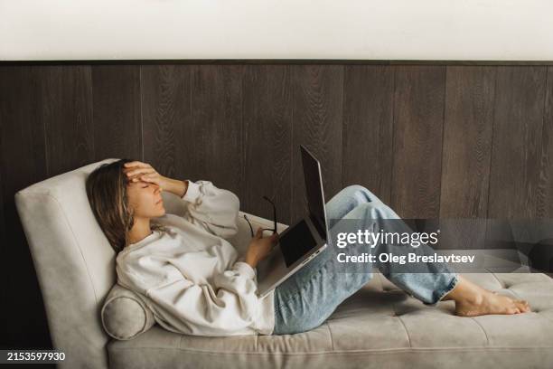 tired woman lying with headache on sofa after work with laptop - midlife crisis stock pictures, royalty-free photos & images