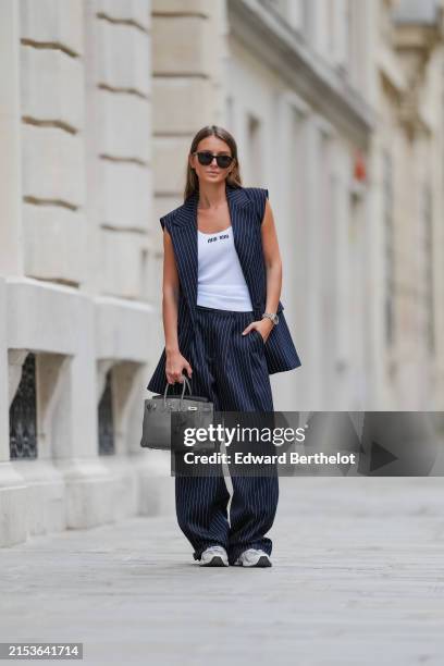 Diane Batoukina wears YSL Saint-Laurent sunglasses, a white t-shirt by Miu Miu, a Rolex watch, a navy blue dark striped suit by The Frankie Shop,...