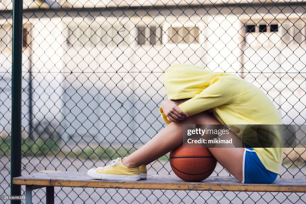 Trauriges Teenager-Mädchen, das mit Basketball auf der Bank sitzt.