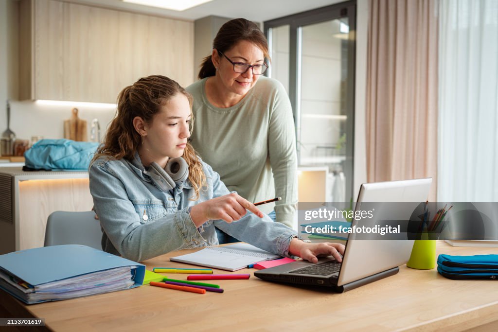Schoolgirl doing homework with her mother. She is having online class using laptop