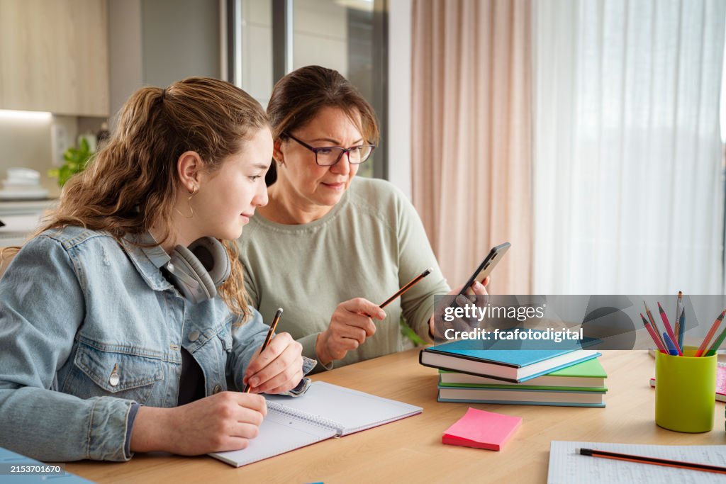 Mother and schoolgirl daugher using phone to do homework