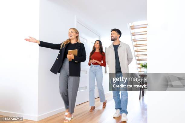 real estate agent showing a young couple a new house. the house is modern and contemporary. - visita de inmuebles en venta fotografías e imágenes de stock