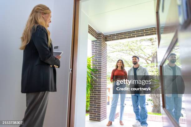 real estate agent showing a young couple a new house. the house is modern and contemporary. - visita de inmuebles en venta fotografías e imágenes de stock