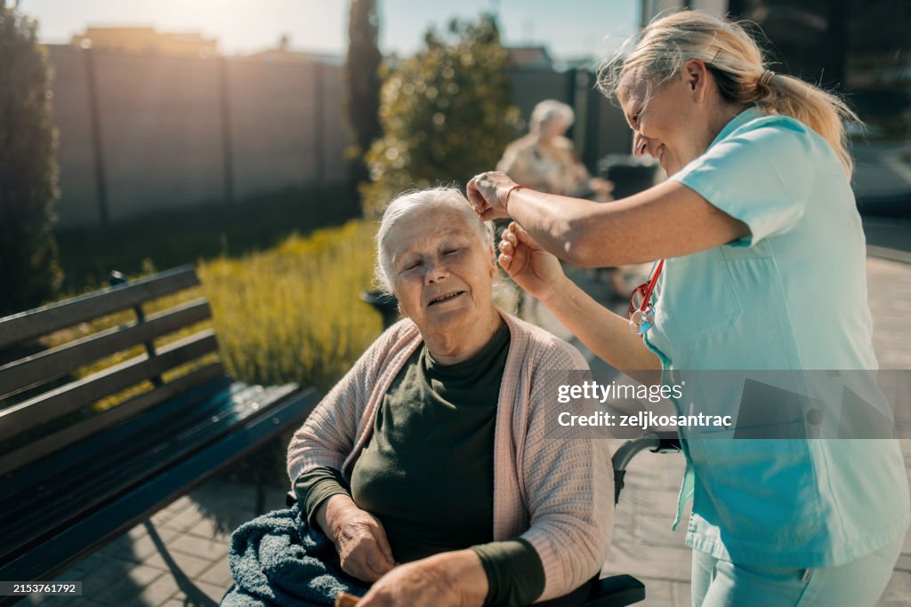 Elderly senior woman on wheelchair with a nurse outdoor in nursing hospital garden
