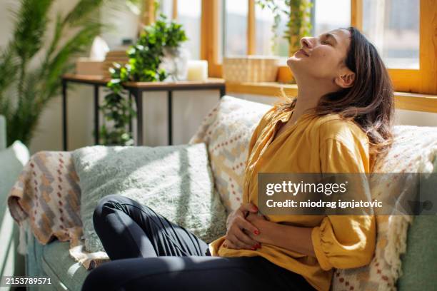 woman experiencing stomach pain at home - spijsverteringsstelsel stockfoto's en -beelden