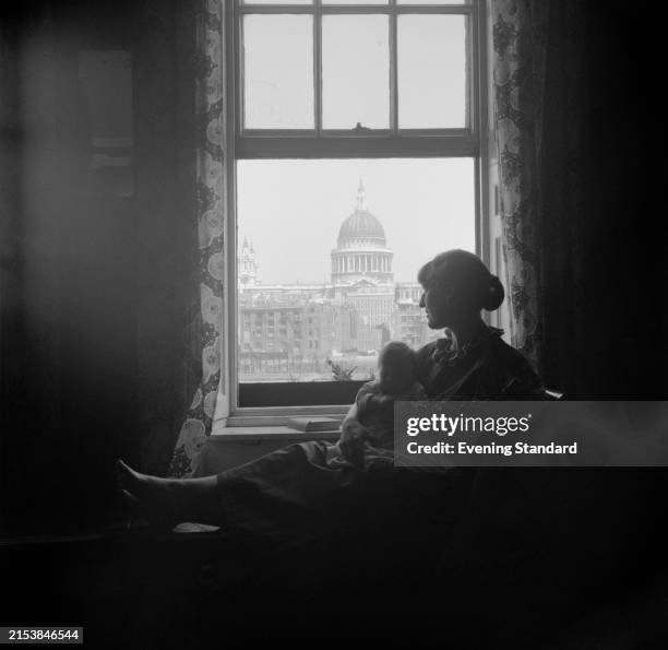 Woman holding a baby looks through a window showing St Paul's Cathedral, London, September 8th 1954.