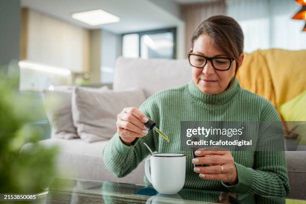 portrait of a woman using a dropper to put medicine into a cup - cbd oil stock pictures, royalty-free photos & images