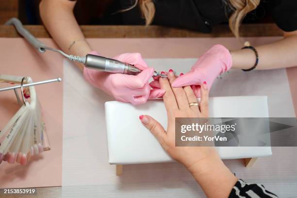 manicurist in pink medical gloves files the cuticle of the client with a hardware file - manicure stockfoto's en -beelden