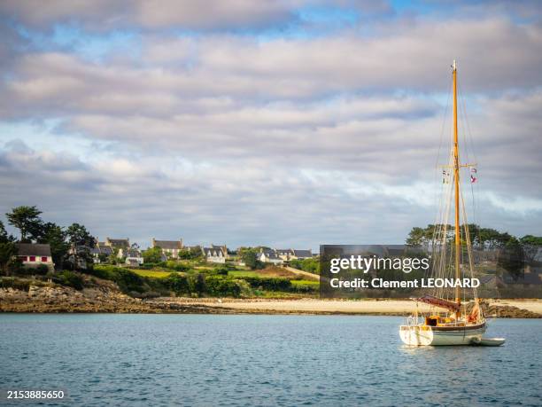 coastline of the batz island at sunset as seen from a boat, with a sailing ship, a white sand beach and typical breton houses, finistère (finistere) - bretagne (brittany) - western france. - finistere stock pictures, royalty-free photos & images