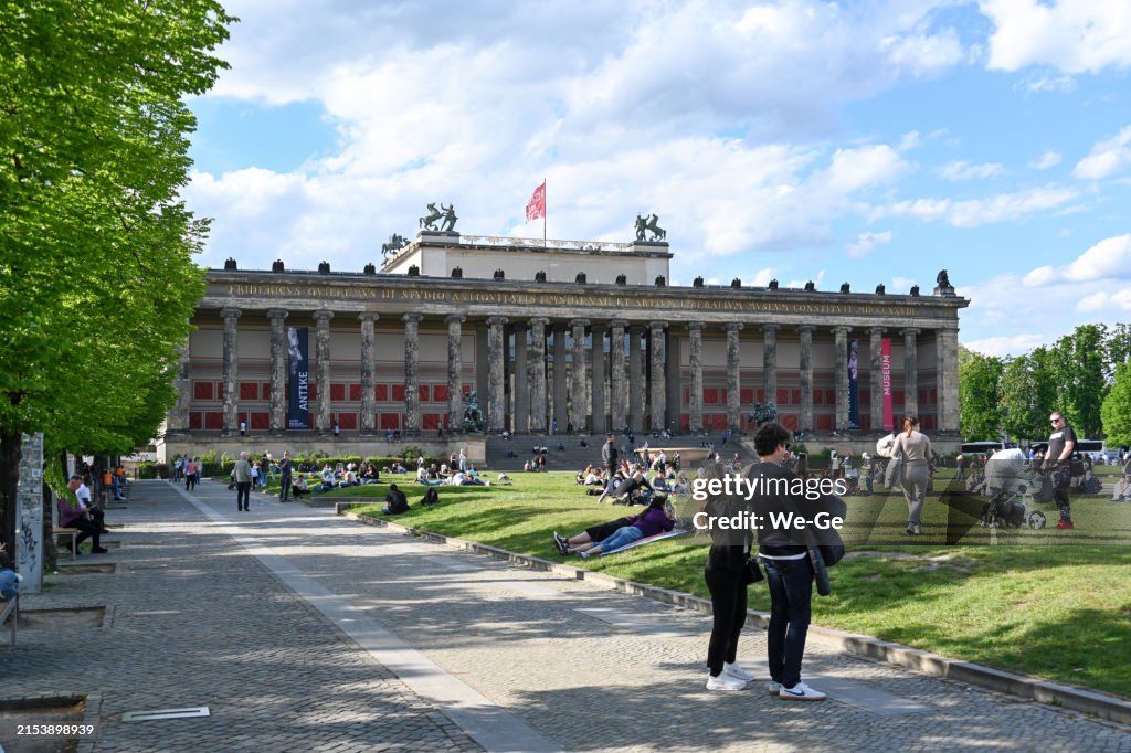Touristen und Einheimische genießen die Sonne auf der Wiese vor dem Alten Museum auf der Museumsinsel in Berlin-Mitte.