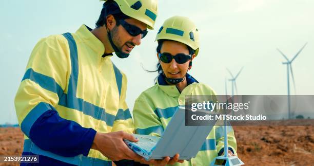 renewable energy engineers holding laptop consulting, collaborate on project in field of wind turbines under clear sky. green ecological power generation wind sustainable energy. - land surveyor stock pictures, royalty-free photos & images