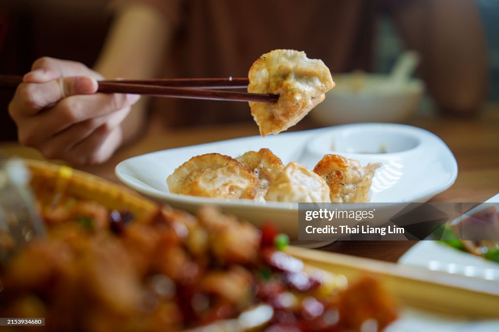 Close up of an Asian woman enjoying freshly served traditional Chinese grilled dumpling with chopsticks in a restaurant