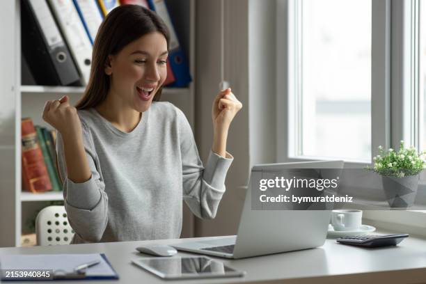 celebrating an achievement while using her laptop - sorte imagens e fotografias de stock
