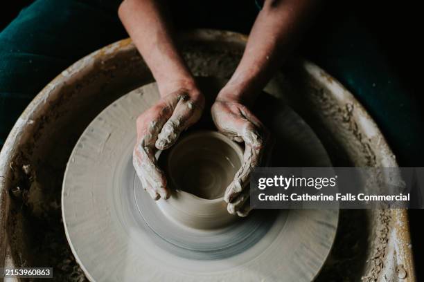 top down image of a womans cupped hands around wet clay on a potters wheel - alfarería fotografías e imágenes de stock