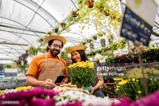 compañeros de trabajo que trabajan y usan el teléfono móvil en el invernadero - mercado de flores fotografías e imágenes de stock