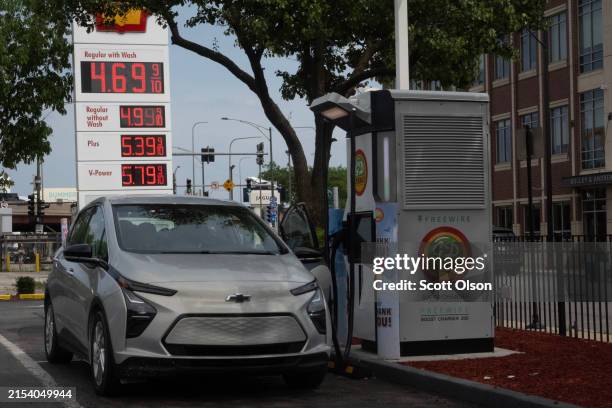 An electric car charges up in front of a sign displaying gas prices at a gas station on May 21, 2024 in Chicago, Illinois. President Joe Biden has...