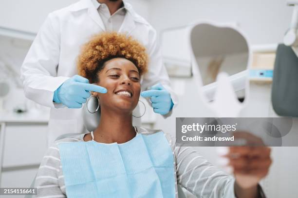 woman in dentist office holding mirror - tandarts stockfoto's en -beelden