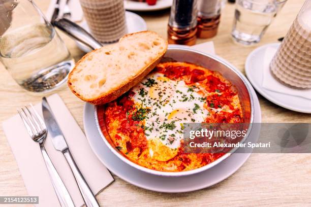 shakshuka served in a skillet with fresh bread at a restaurant, close-up - cucina del medio oriente foto e immagini stock
