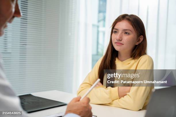 une adolescente consulte un médecin dans la salle d’examen de l’hôpital. le médecin enregistre ses antécédents médicaux sur un formulaire. moment de soins attentifs et d’interaction professionnelle, mettant en valeur l’environnement de soutie - blouse dexamen médical photos et images de collection