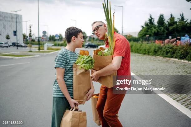 père et fils après avoir fait les courses en portant des sacs en papier vers la voiture et en s’amusant - sachet en papier photos et images de collection