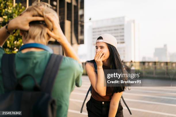 dos jóvenes disfrutando mientras pasan el rato al aire libre en la ciudad - mano tapando la boca fotografías e imágenes de stock