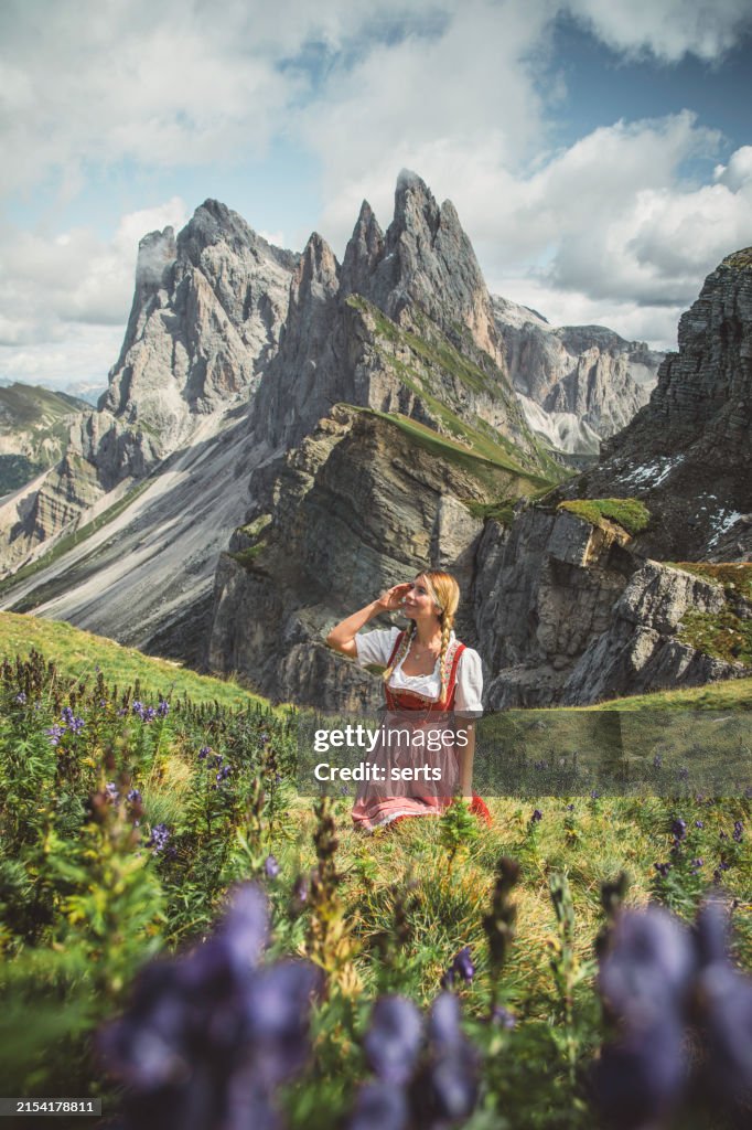 Woman in Traditional Red and White Clothing Enjoying Nature Among Purple Wolfsbane Flowers at Seceda, Dolomites