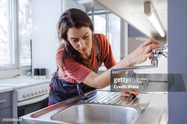 a female plumber works to restore the functionality of the sink and faucet - heraustropfen stock-fotos und bilder