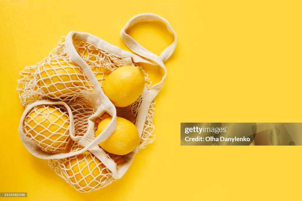Close-up of fresh lemons in reusable shopping bag on yellow background