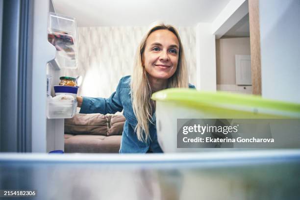 woman looking into a refrigerator and smiling. inside view of a refrigerator with food containers. - refrigerator stock pictures, royalty-free photos & images