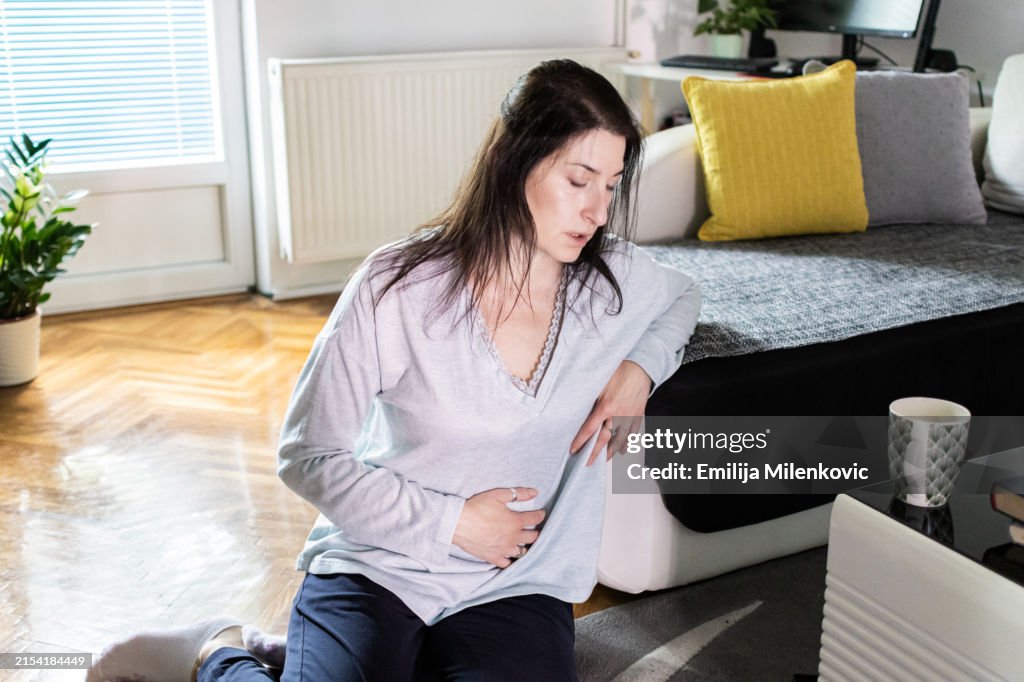 Women with uterine fibroids. Woman is suffering from stomach ache at home. Abdominal pain. Menstrual period, food poisoning, gastritis, diarrhea, feeling unwell sitting in living room.