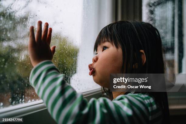 asian toddler girl looking through window glass with raindrops - boring girl stock pictures, royalty-free photos & images