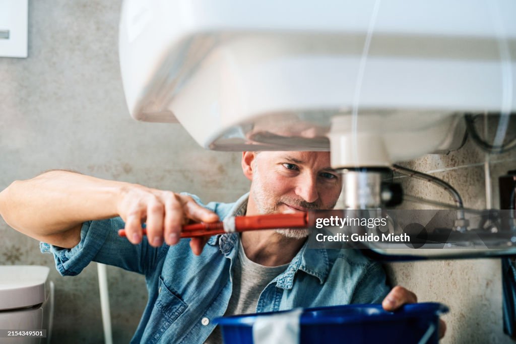 Man trying to fix a leak in a sink using a pipe wrench.