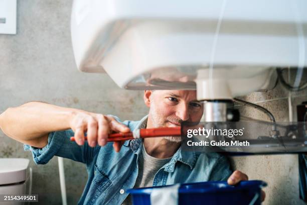man trying to fix a leak in a sink using a pipe wrench. - loodgieter stockfoto's en -beelden