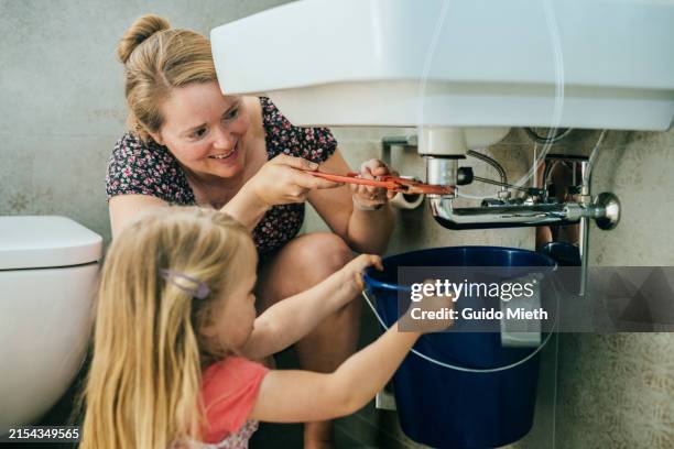 woman trying to fix a leak in a sink using a pipe wrench and her daughter helping. - abfluss stock-fotos und bilder