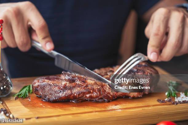 men's hands holding knife and fork, cutting grilled steak - steakhouse table stock pictures, royalty-free photos & images
