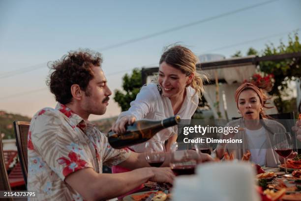 il padrone di casa riempie gioiosamente uno dei suoi ospiti con vino rosso - ricaricare foto e immagini stock