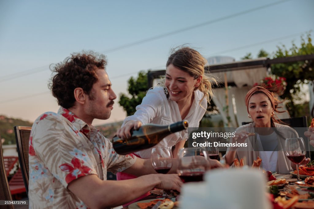 Host joyfully refilling one of her guests glass with red wine