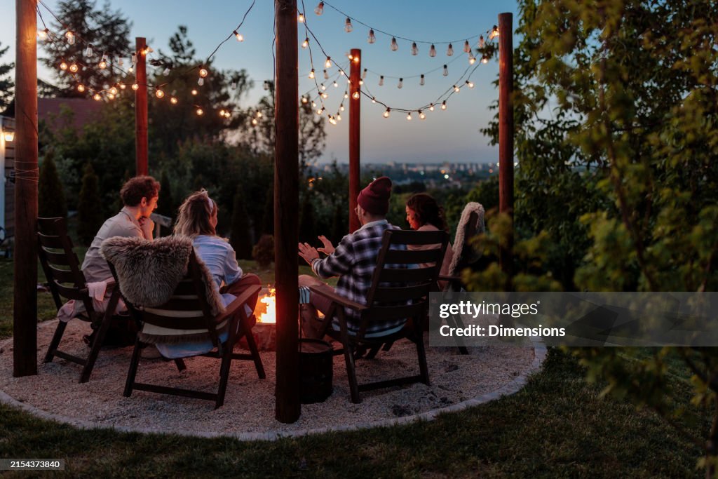 Four people sitting next to a burning fire pit at sunset