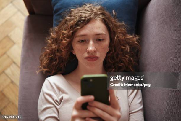 sad lonely gen z girl lying on sofa with phone, scrolling social media, internet addiction - message sms photos et images de collection