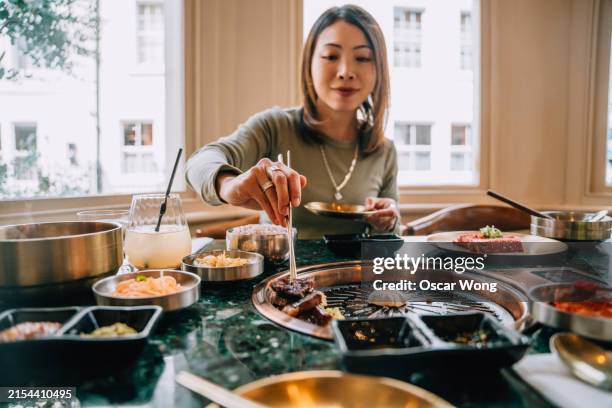 young asian woman enjoying korean barbecue (gogigui) in restaurant - korean culture stock pictures, royalty-free photos & images