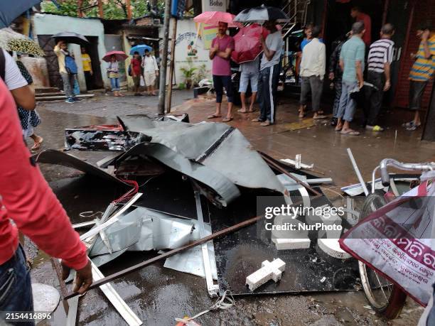 People are standing in front of a damaged billboard during the heavy rain and wind due to cyclone Remal in Kolkata, India, on May 27, 2024.