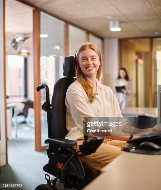 giovane donna disabile che lavora alla sua scrivania in un ufficio - sedia a rotelle foto e immagini stock