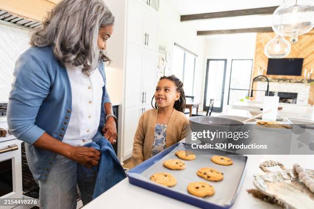 young girl smiles while asking her grandmother if she can have a warm cookie - bakplåt bildbanksfoton och bilder