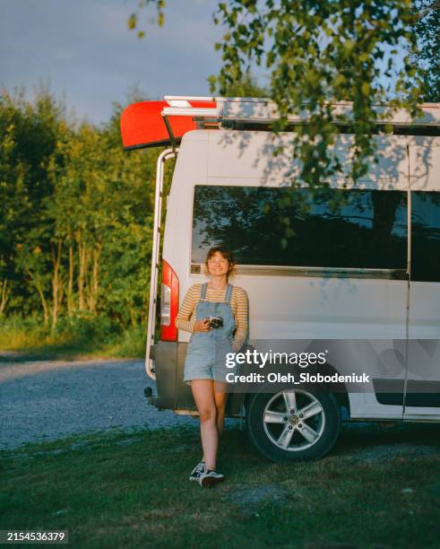 woman with film camera standing near camper van ready to capture memories during road trip - caravan stockfoto's en -beelden